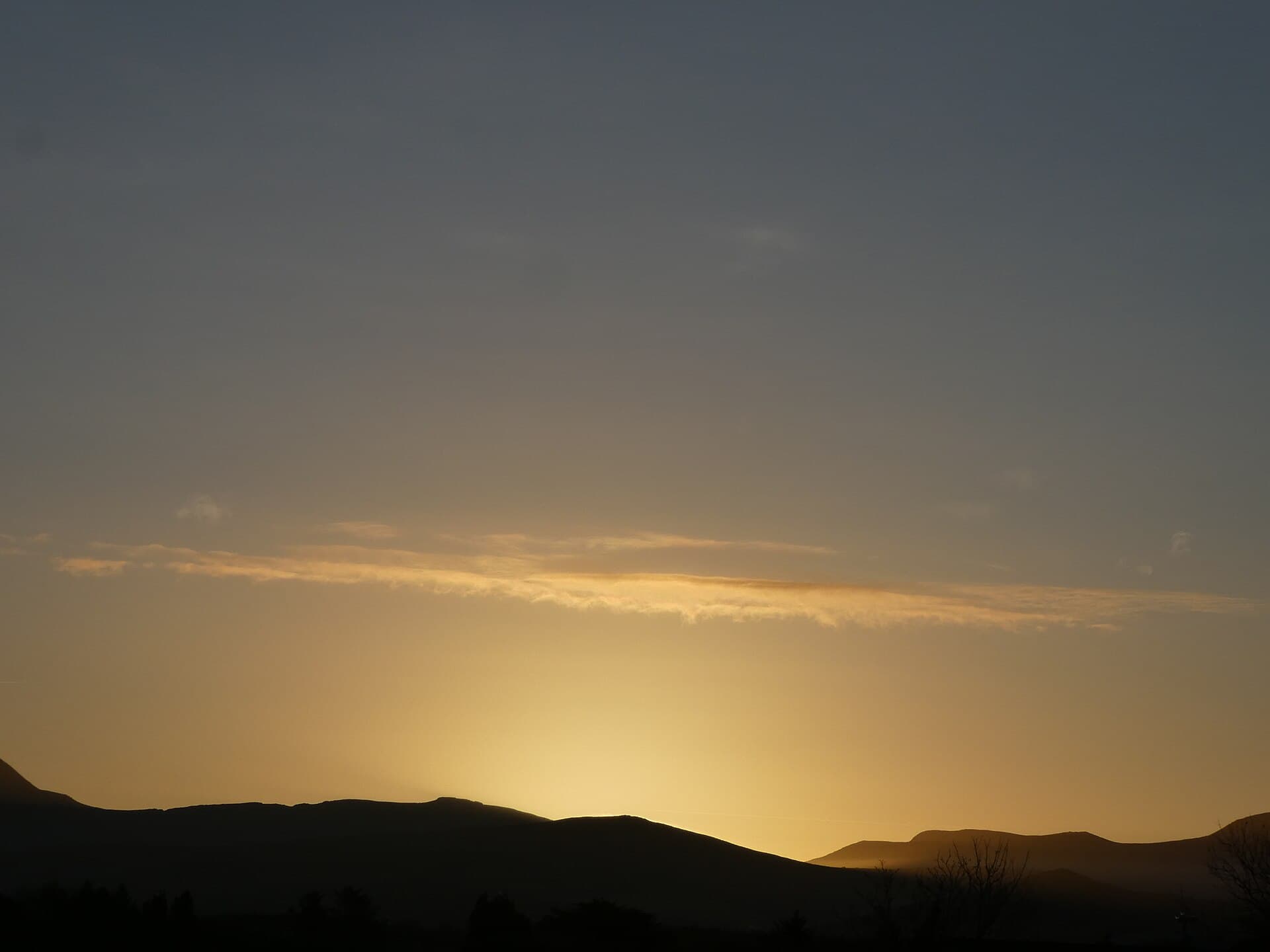 Winter dawn over distant hills, with pale light along the horizon.