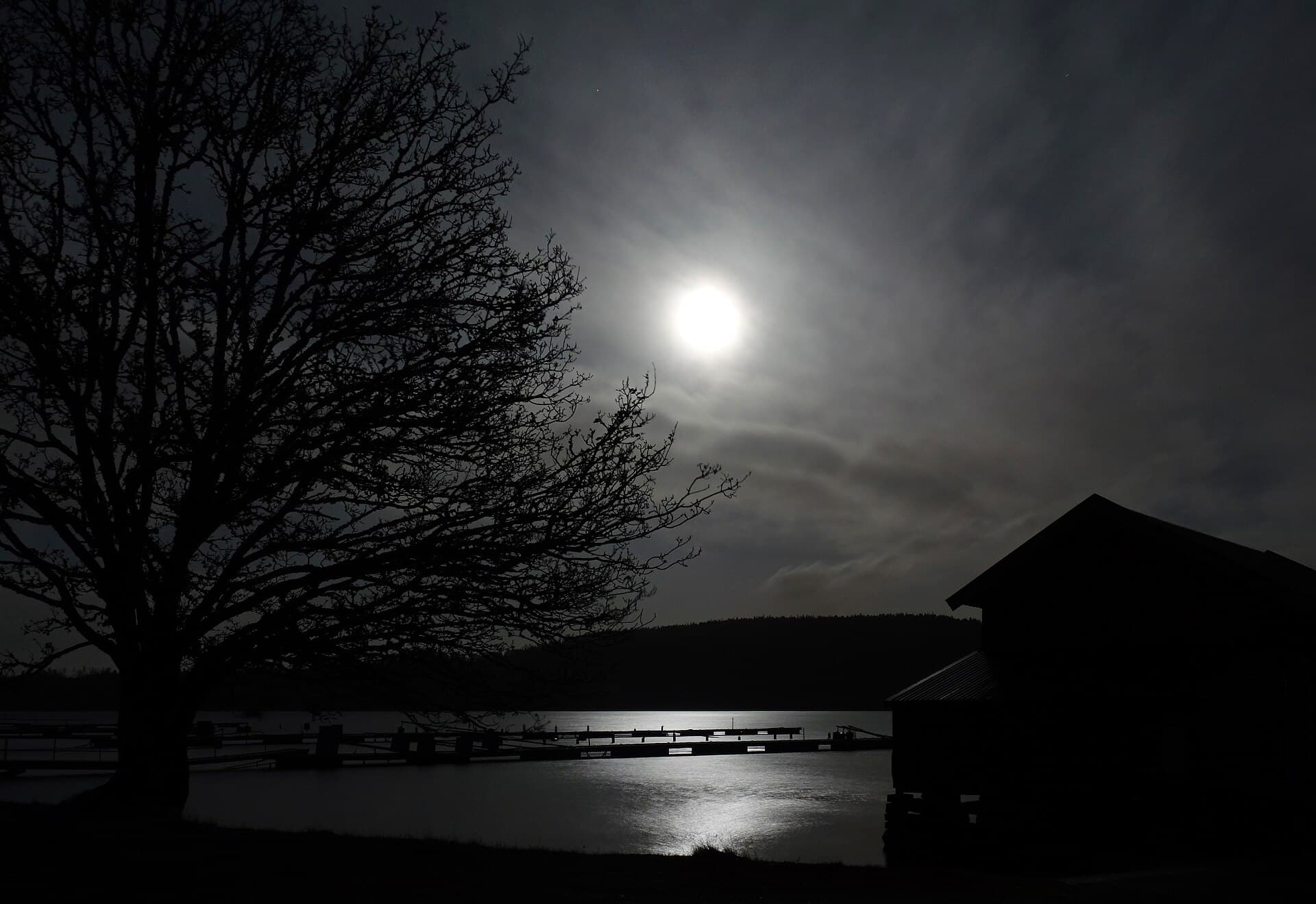 A full moon shining through cloud over dark water.